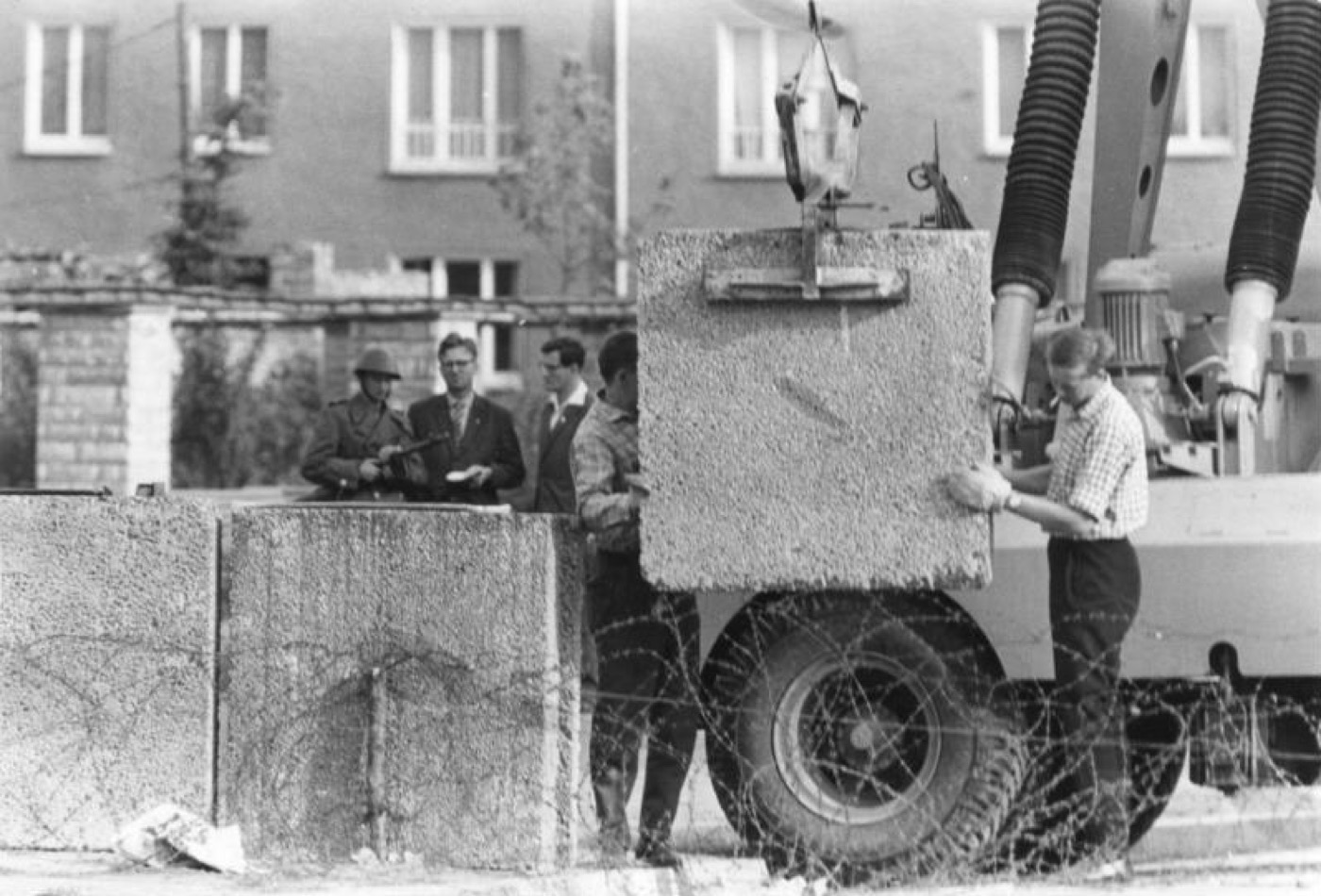 Construction of the Berlin Wall in August 1961 — a crane lowers concrete blocks into place behind barbed wire as soldiers stand watch