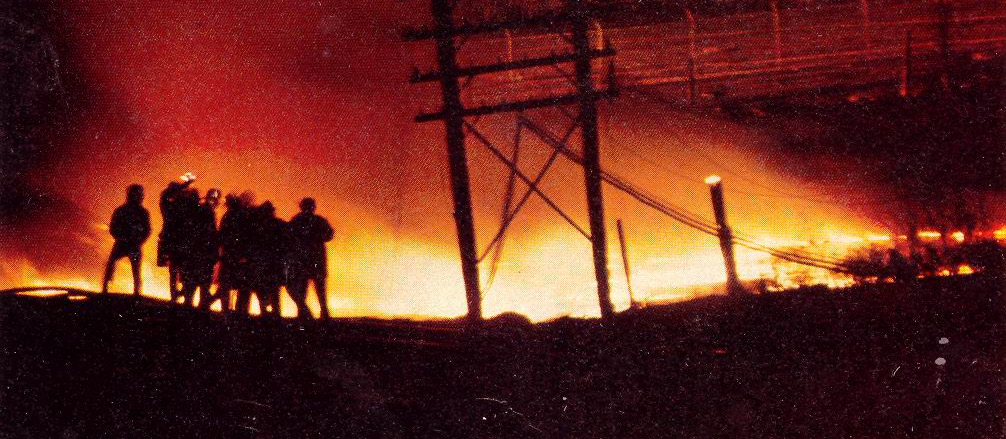 Silhouettes of firefighters and emergency responders against an orange sky lit by the burning propane tankers at the Mississauga derailment